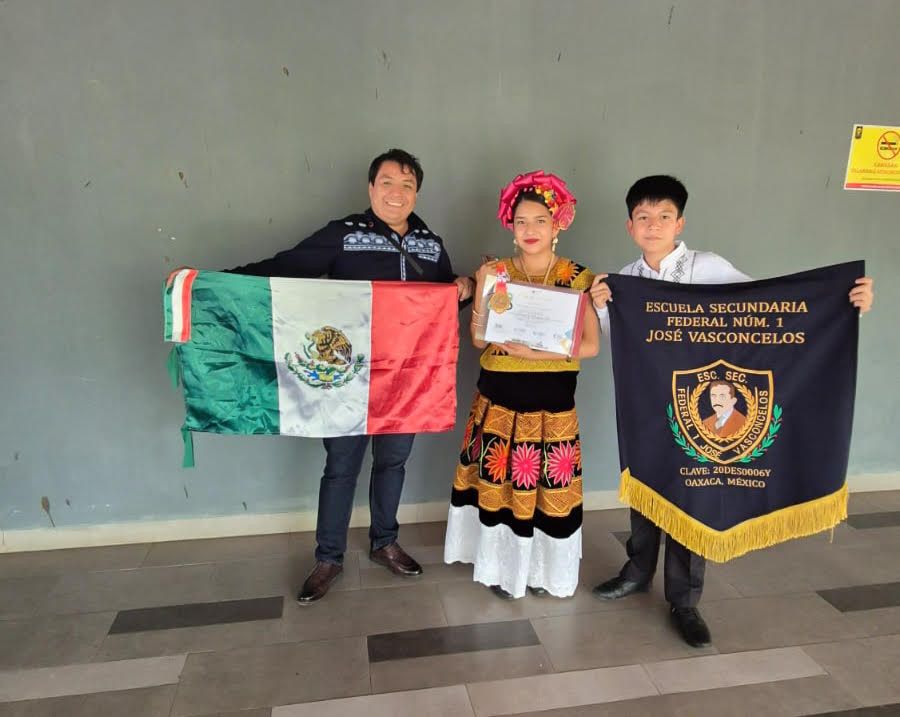 El profesor Francisco Javier Cruz Hernández con la bandera de México, junto a Vioreny Revilla Miranda en traje regional del Istmo y Brayan David Gordillo Santiz con el estandarte de la Escuela Secundaria Federal Núm. 1 José Vasconcelos