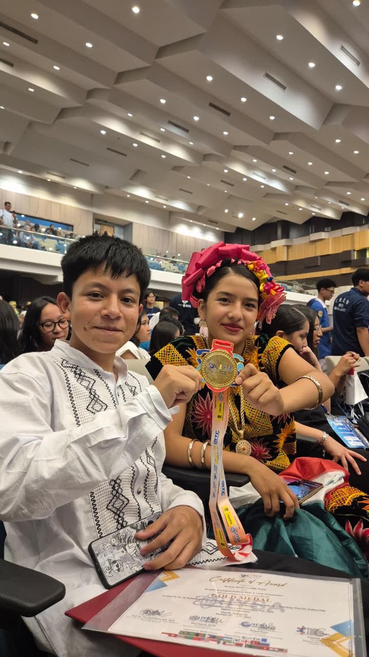 Brayan y Vioreny, en traje regional, muestran una medalla de oro y su certificado en el auditorio